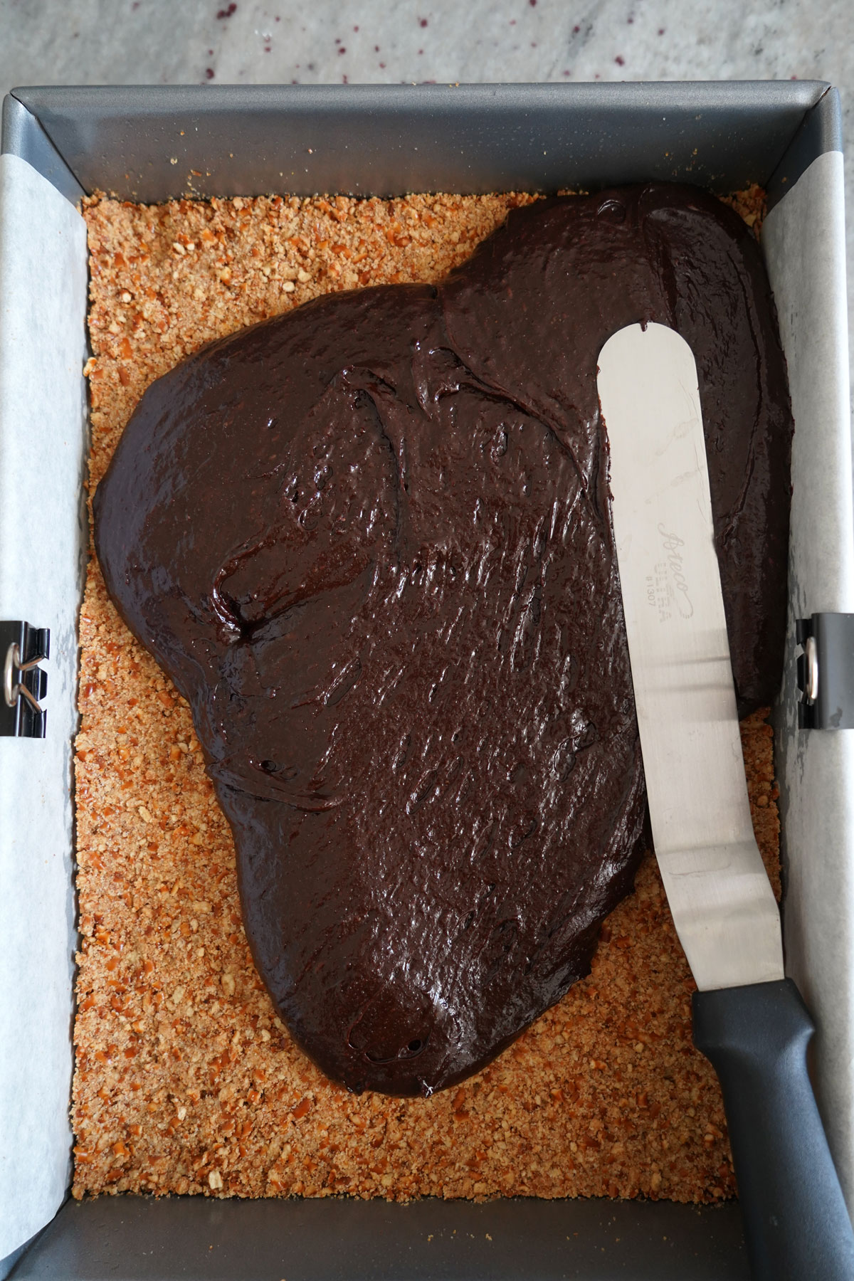 Brownie batter being spread over baked pretzel crust.