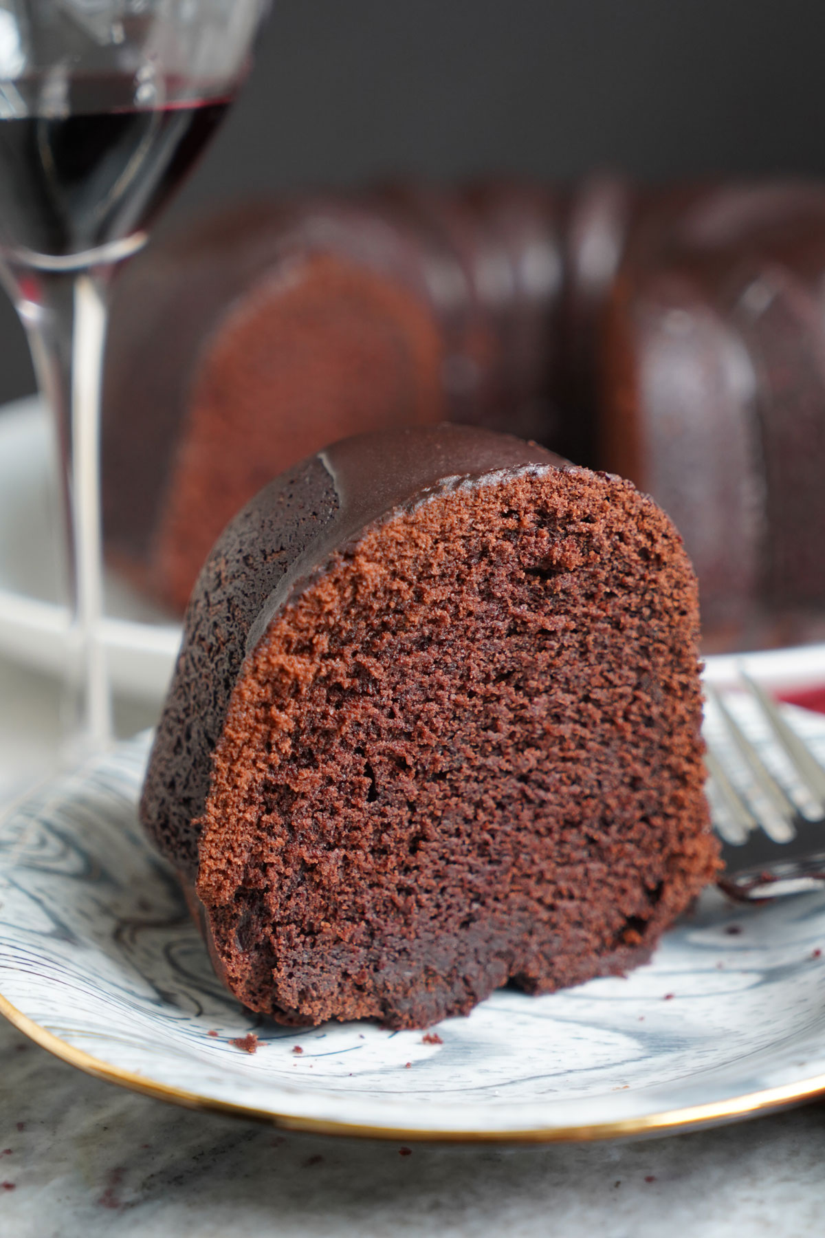 Slice of cake on plate with glass of red wine.