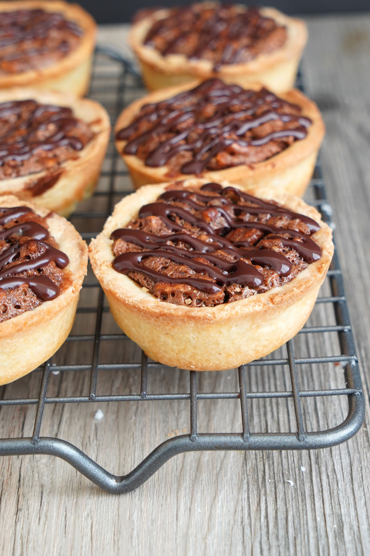 Mini Pecan pies on cooling rack, drizzled with chocolate.