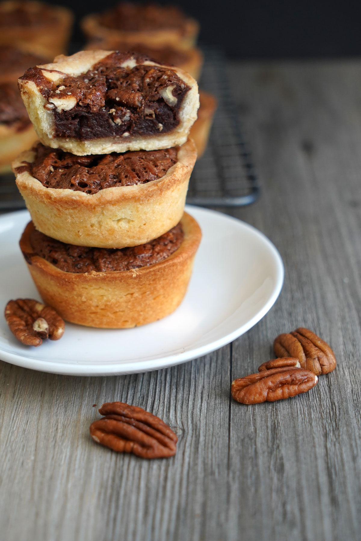 Three mini pecan pies stacked on a plate with top pie cut in half to show filling.
