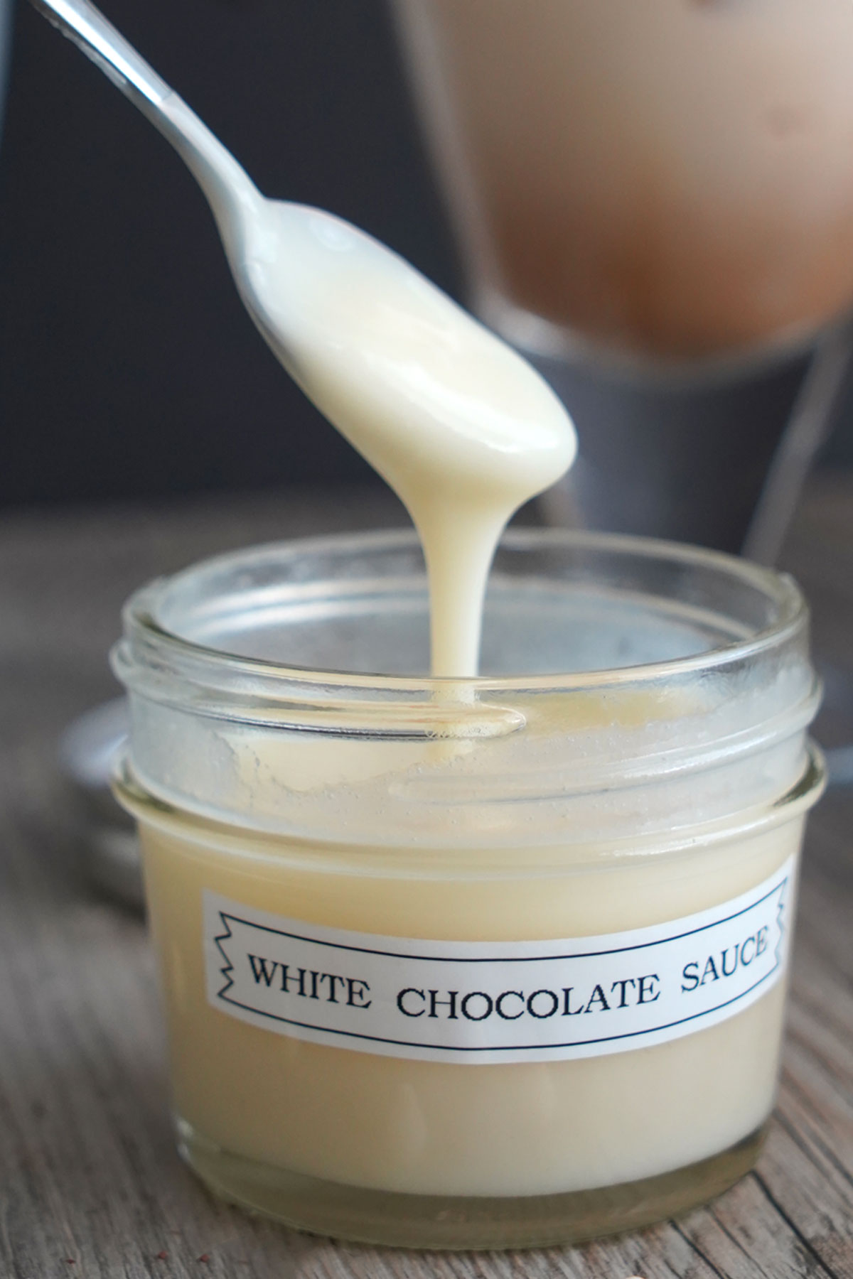 Homemade white chocolate sauce in a small glass jar. Dripping from spoon into jar.