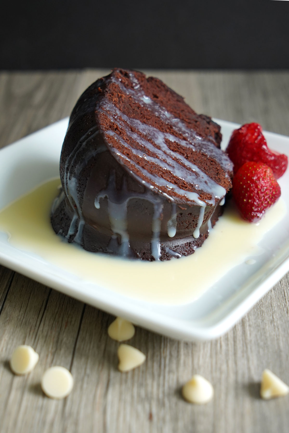 Chocolate cake in a pool of white chocolate sauce on a white plate with berry garnish.