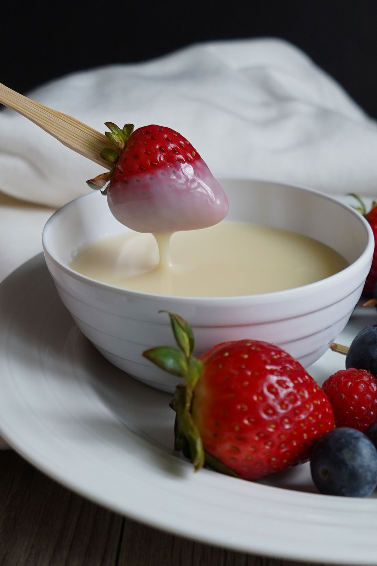 Strawberry being dipped into white chocolate sauce.