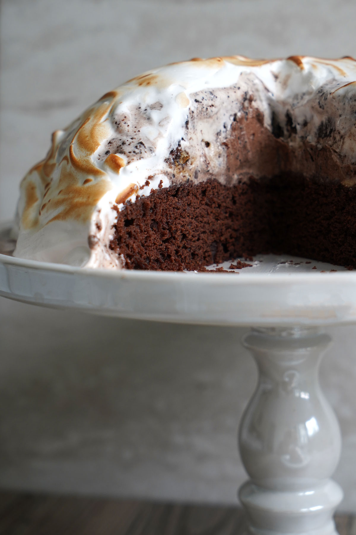 Baked Alaska on white pedestal. Cake is sliced to show ice cream inside.