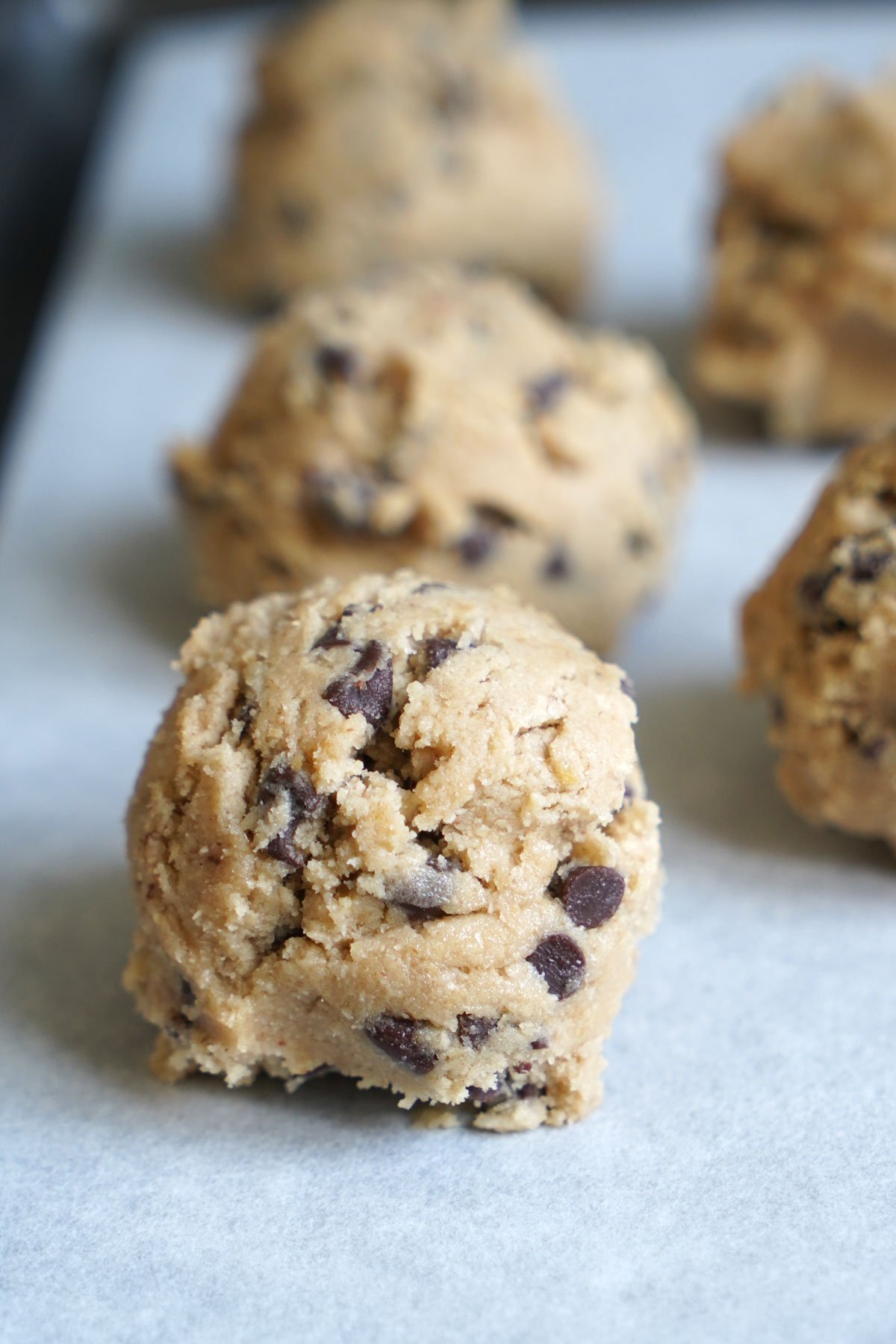 Baking tray lined with parchment paper holding scooped balls of edible cookie dough.

