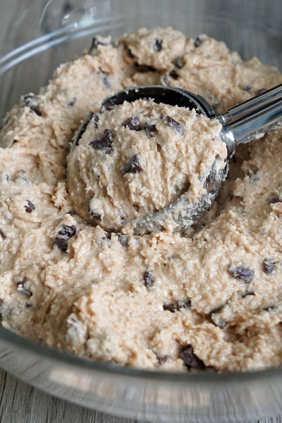 Ice cream scoop lifting a portion of eggless cookie dough from a mixing bowl.