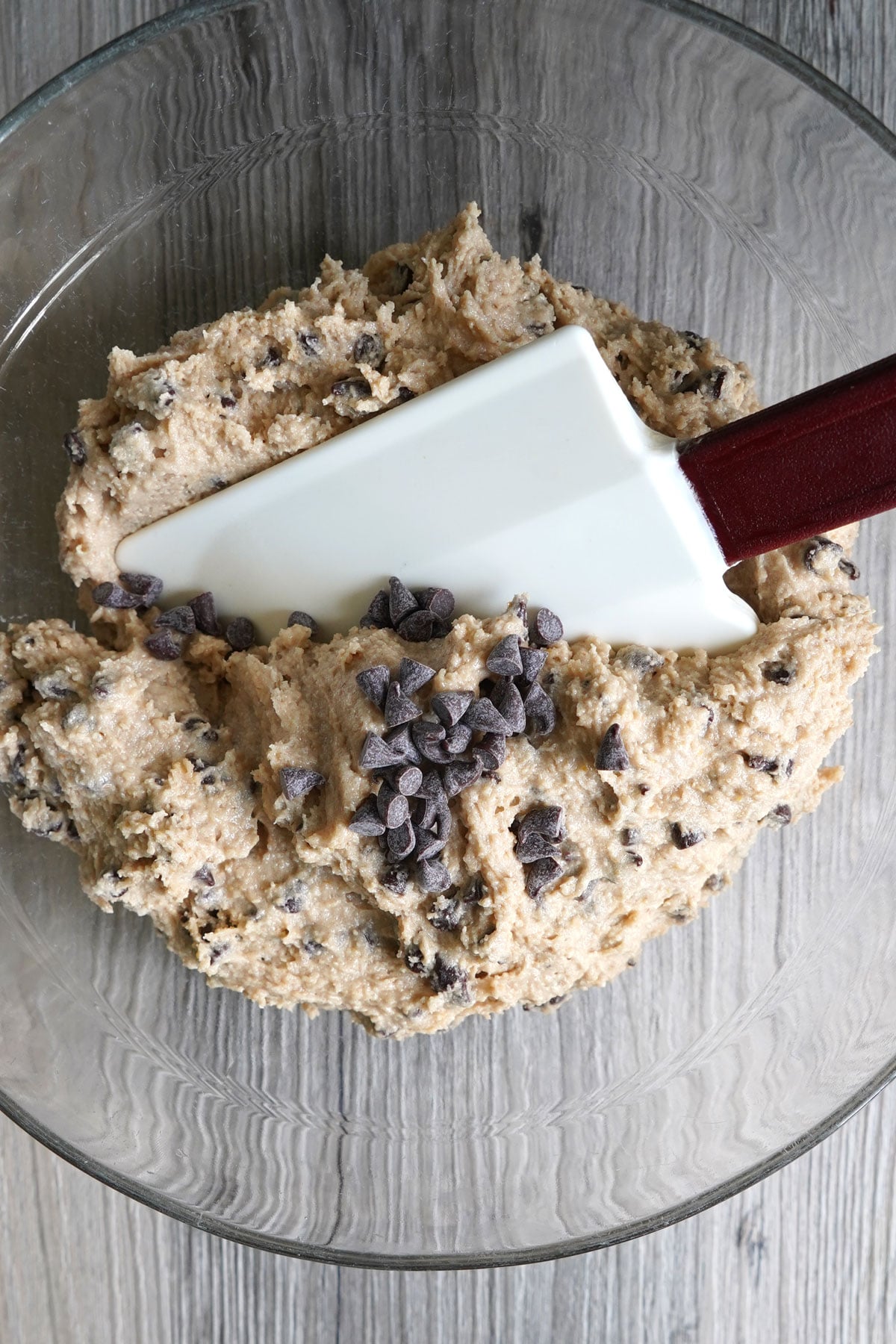Mixing bowl with spatula stirring mini chocolate chips into eggless cookie dough.