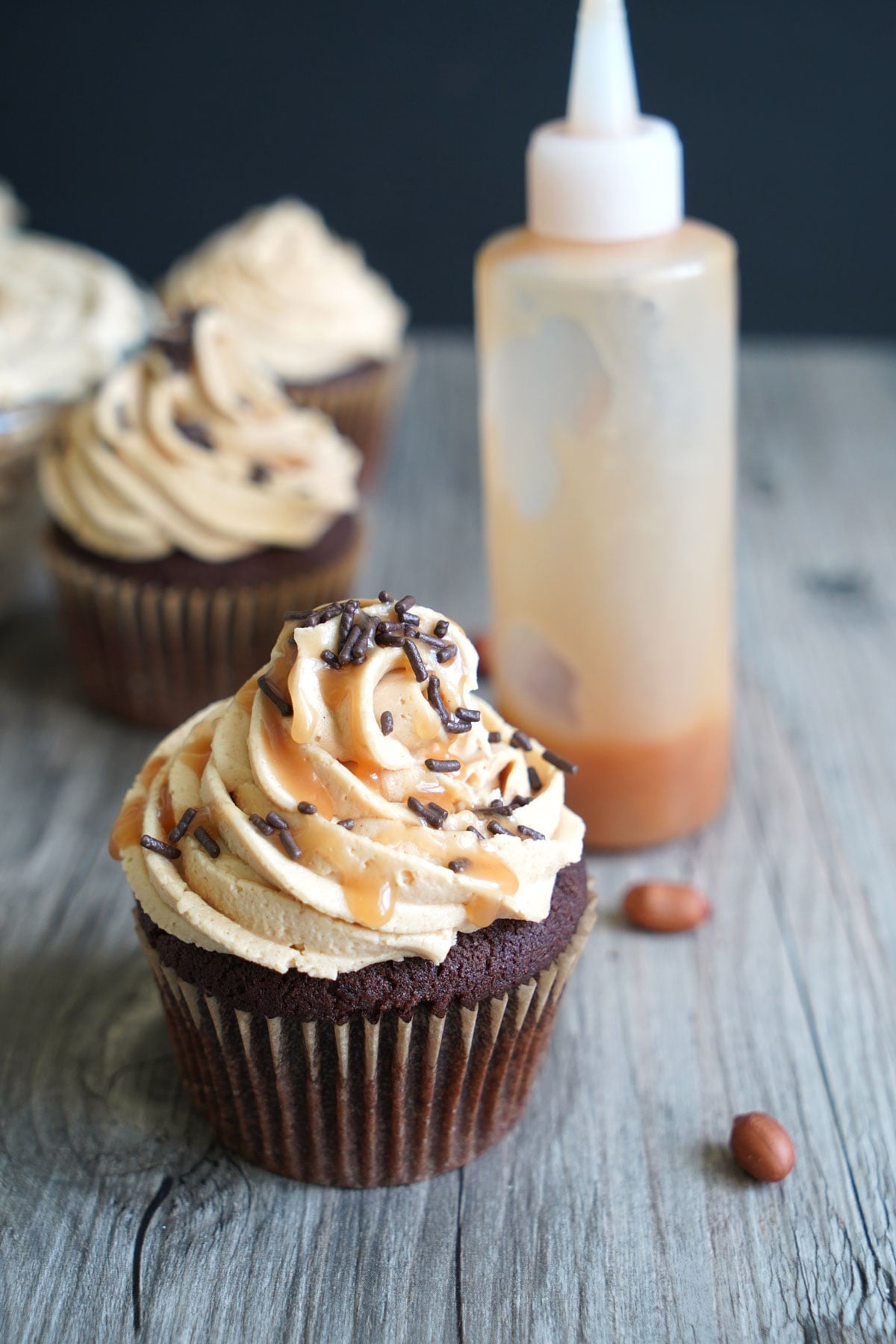 Chocolate cupcake with peanut butter frosting topped with chocolate sprinkles and a drizzle of caramel sauce.