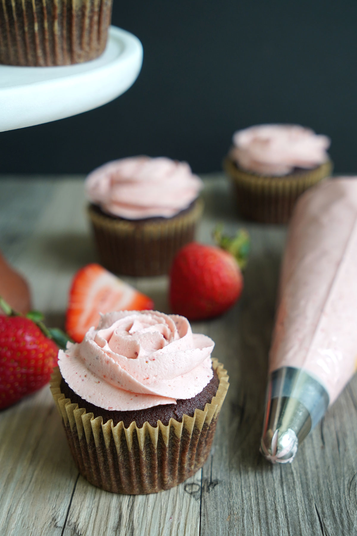 Chocolate cupcake topped with strawberry buttercream with piping bag off to the side. 