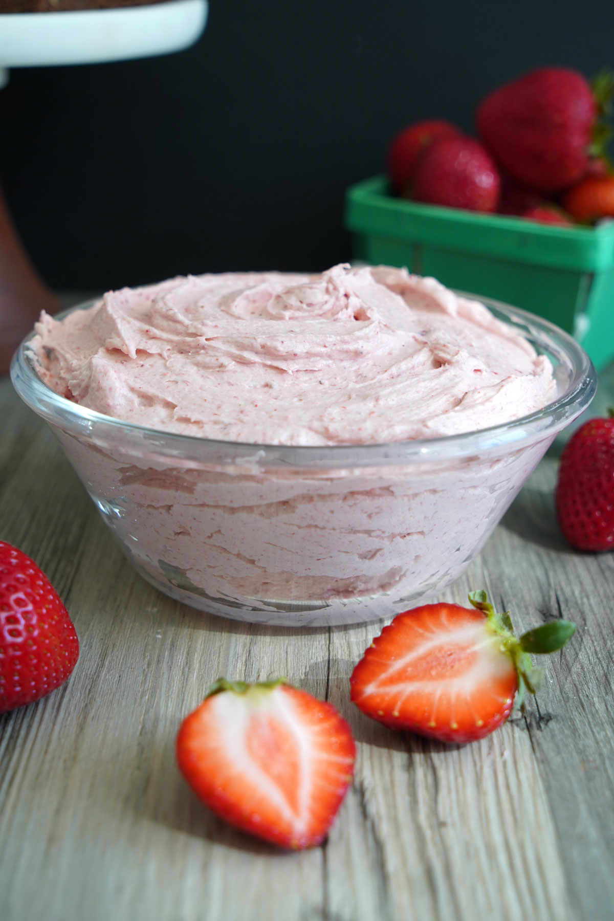 Strawberry buttercream frosting in a glass bowl, surrounded by fresh strawberries.