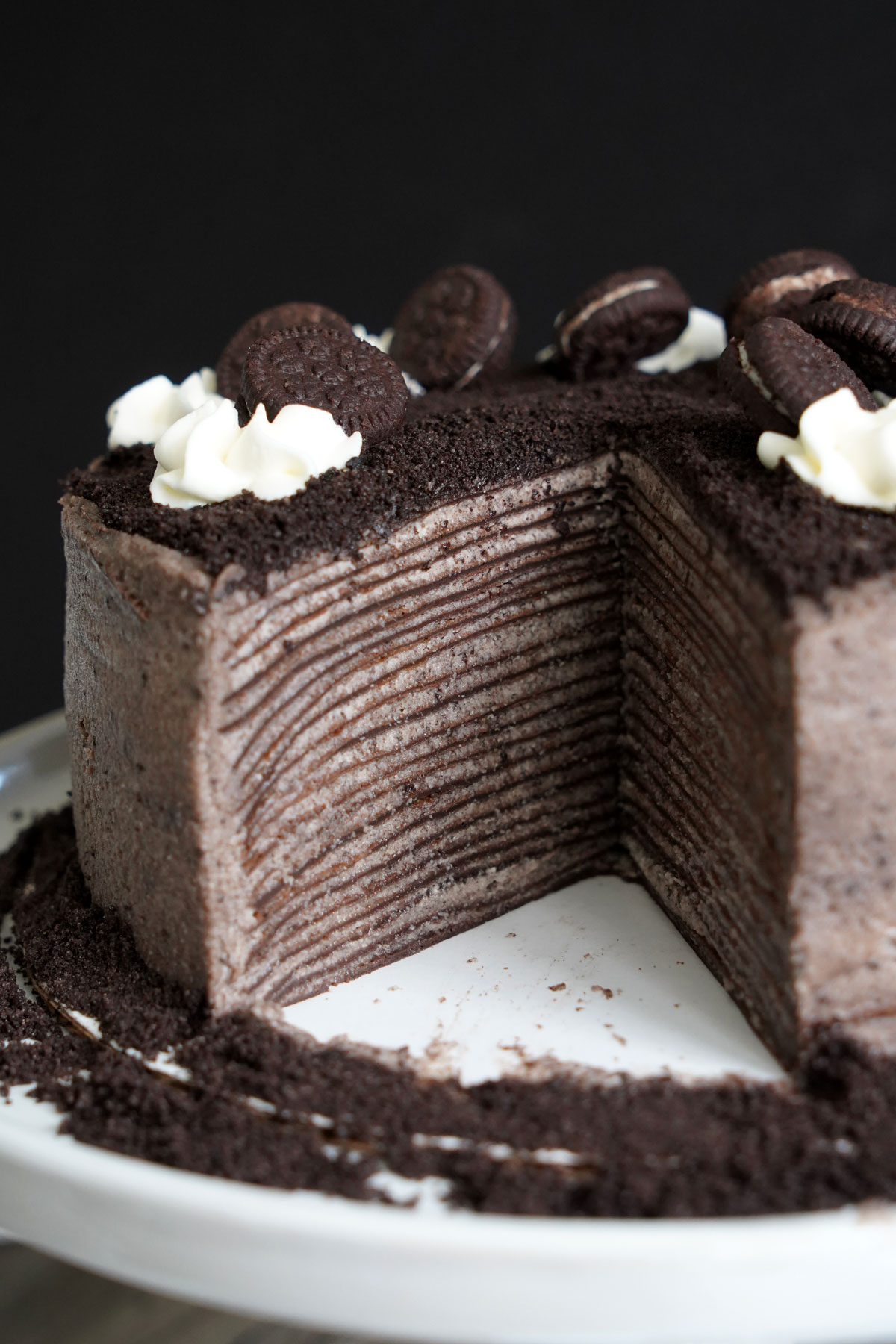 Oreo  crepe cake with slice cut out showing layers or crepes with cookies and cream filling.