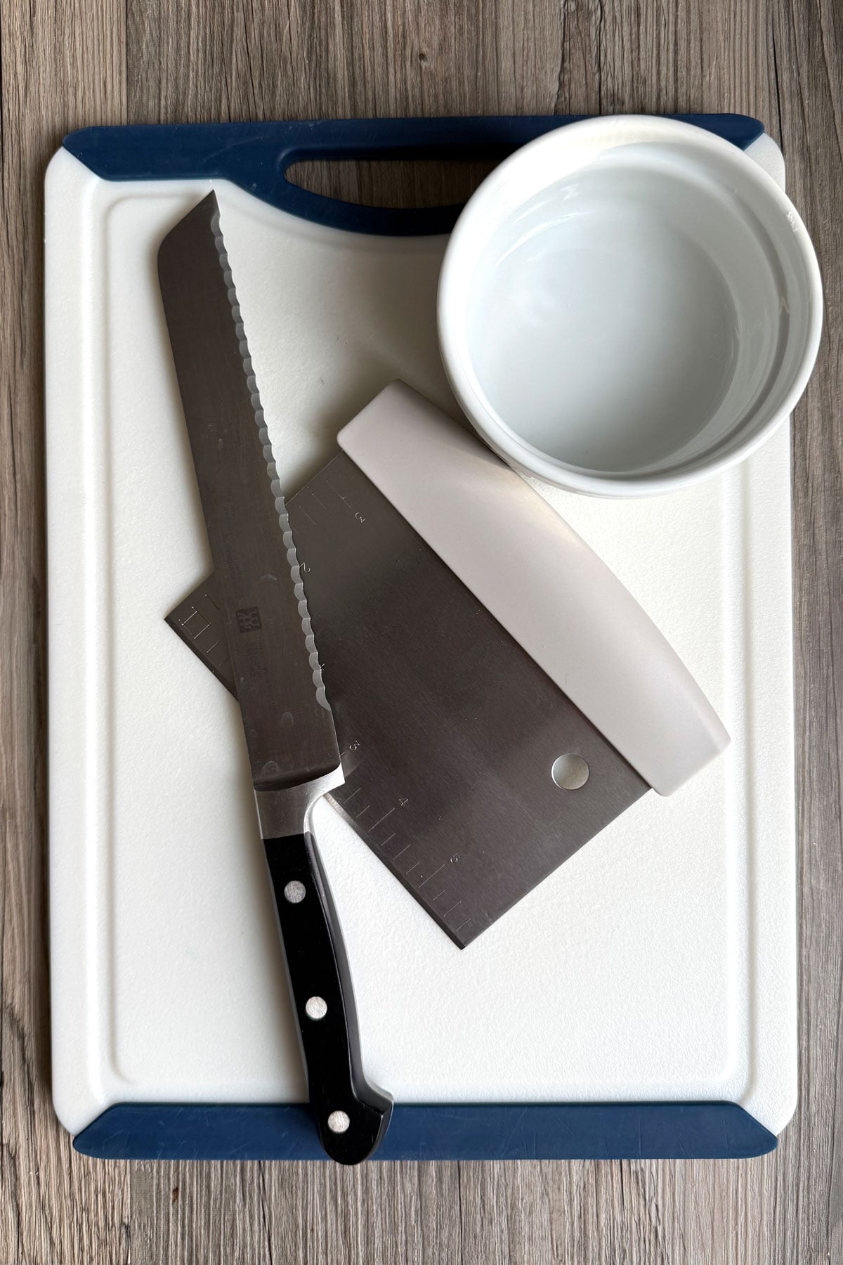 Equipment needed to chop chocolate: cutting board, serrated knife, bench scraper and empty bowl.