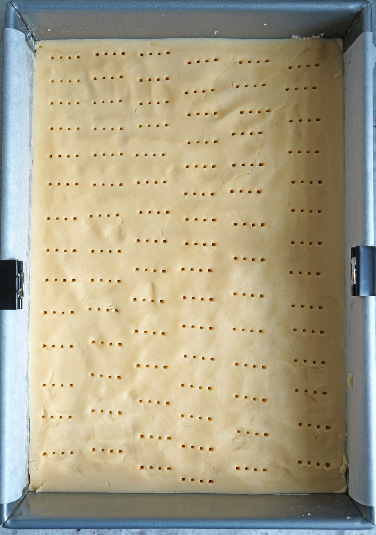Shortbread cookie dough pressed into a pan with holes poked thrroughout. 