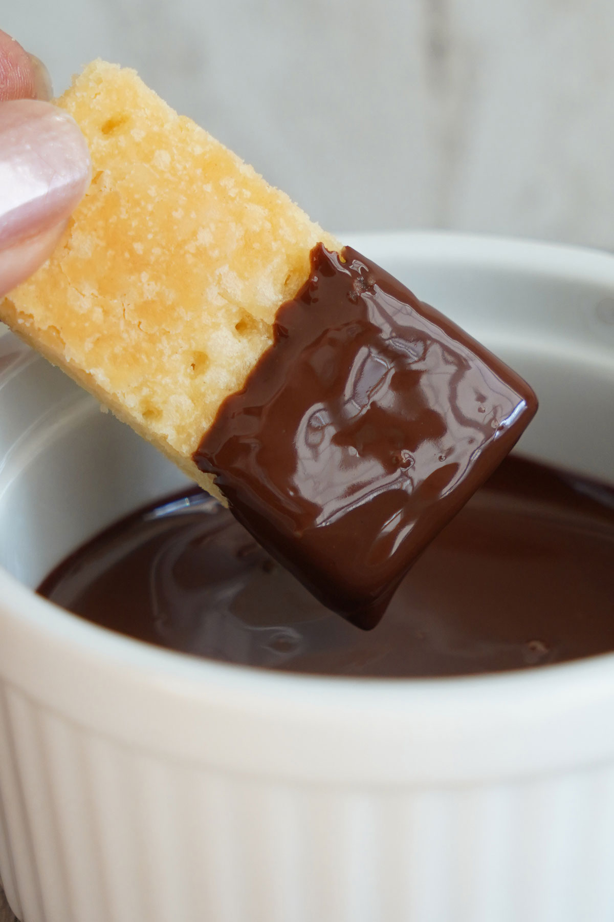 Shortbread cookie being dipped in tempered chocolate. 