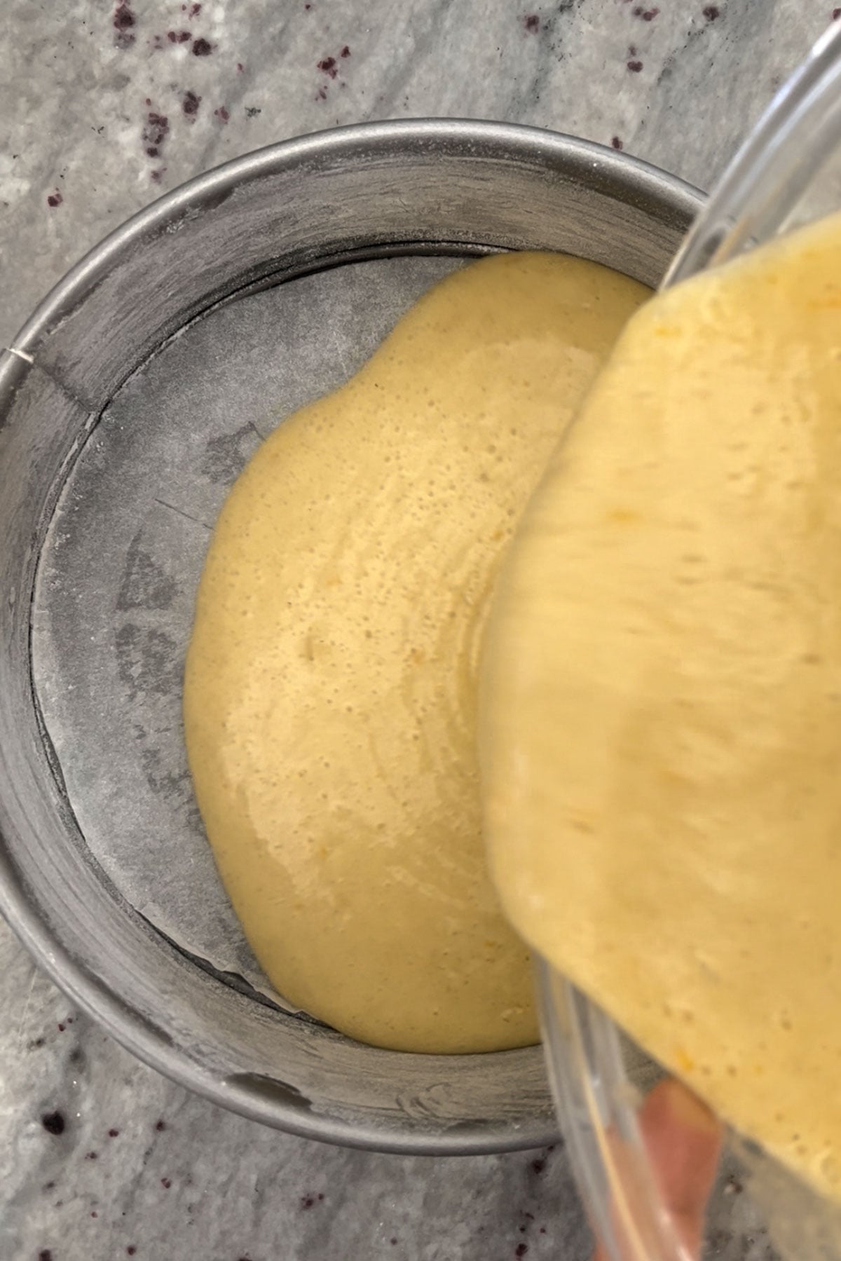 Pouring batter of orange cardamom olive oil cake into prepared pan.