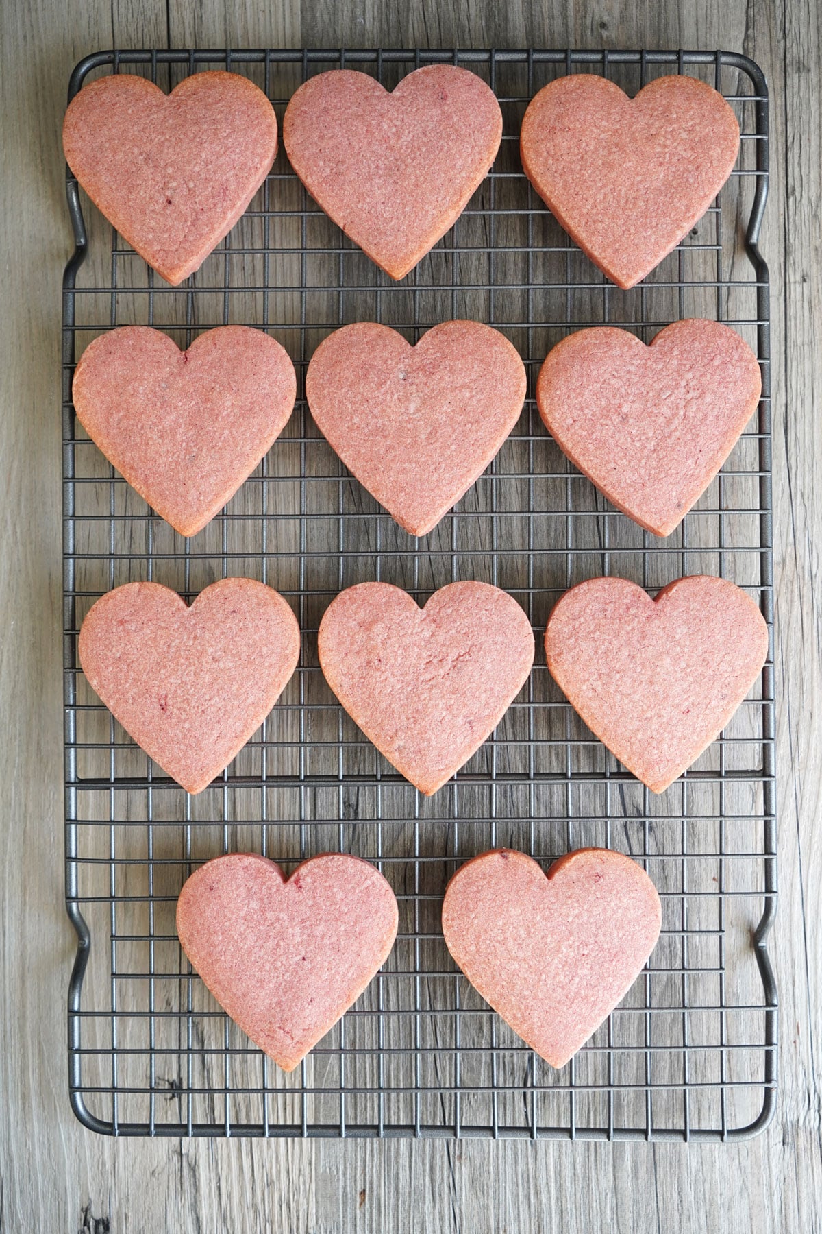 Heart shaped cookies made with pink dough cooling on rack.