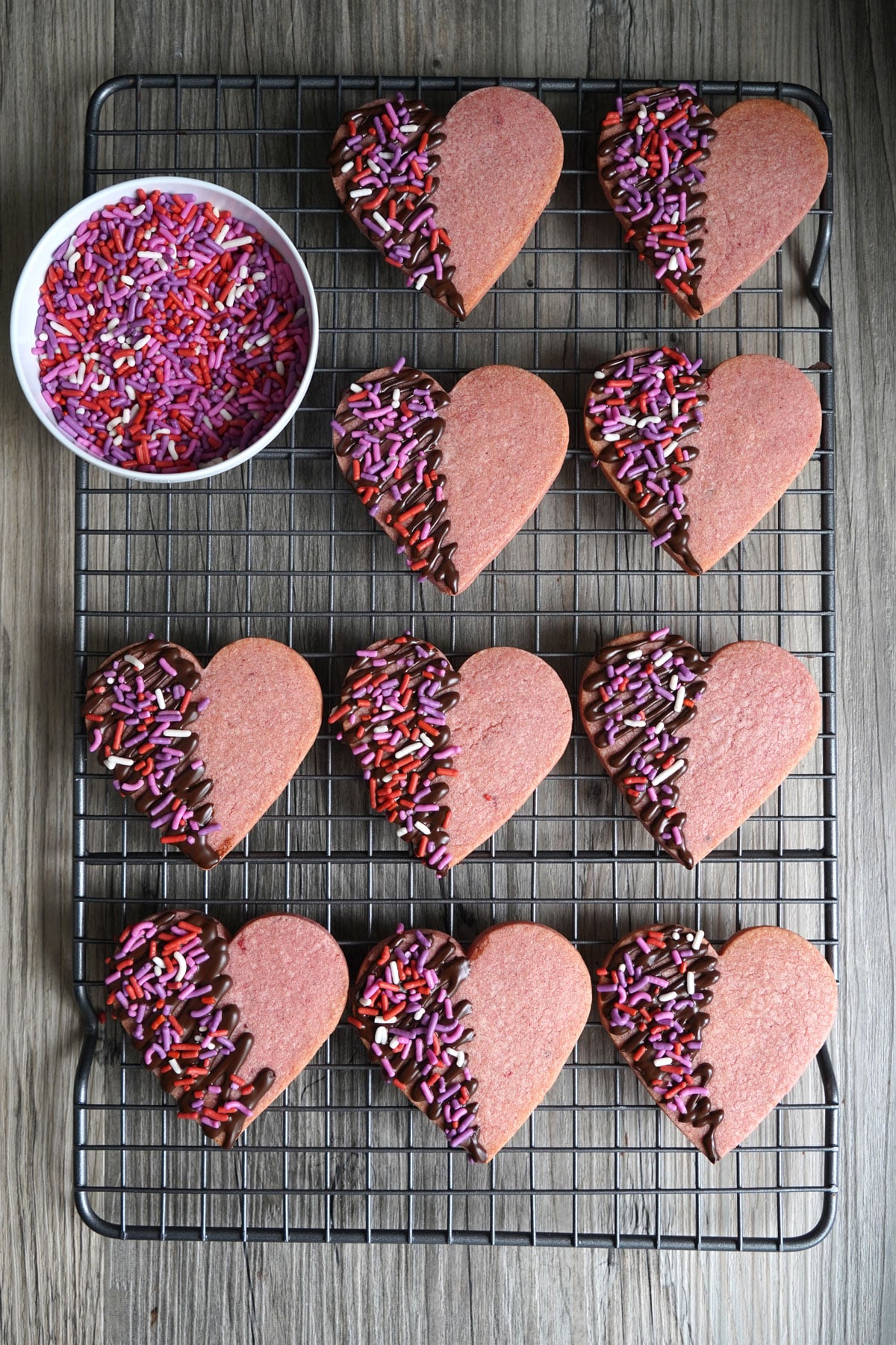 Heart shaped cookies drying after being decorated with chocolate and sprinkles.