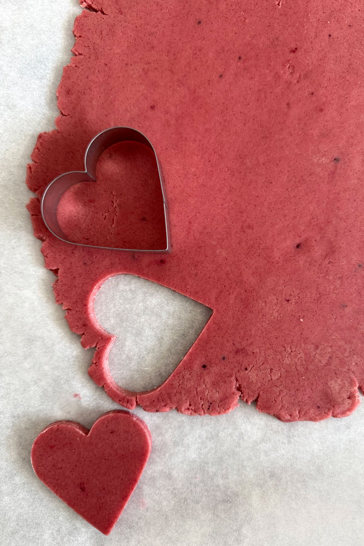 Heart shapes being cut out of pink cookie dough.