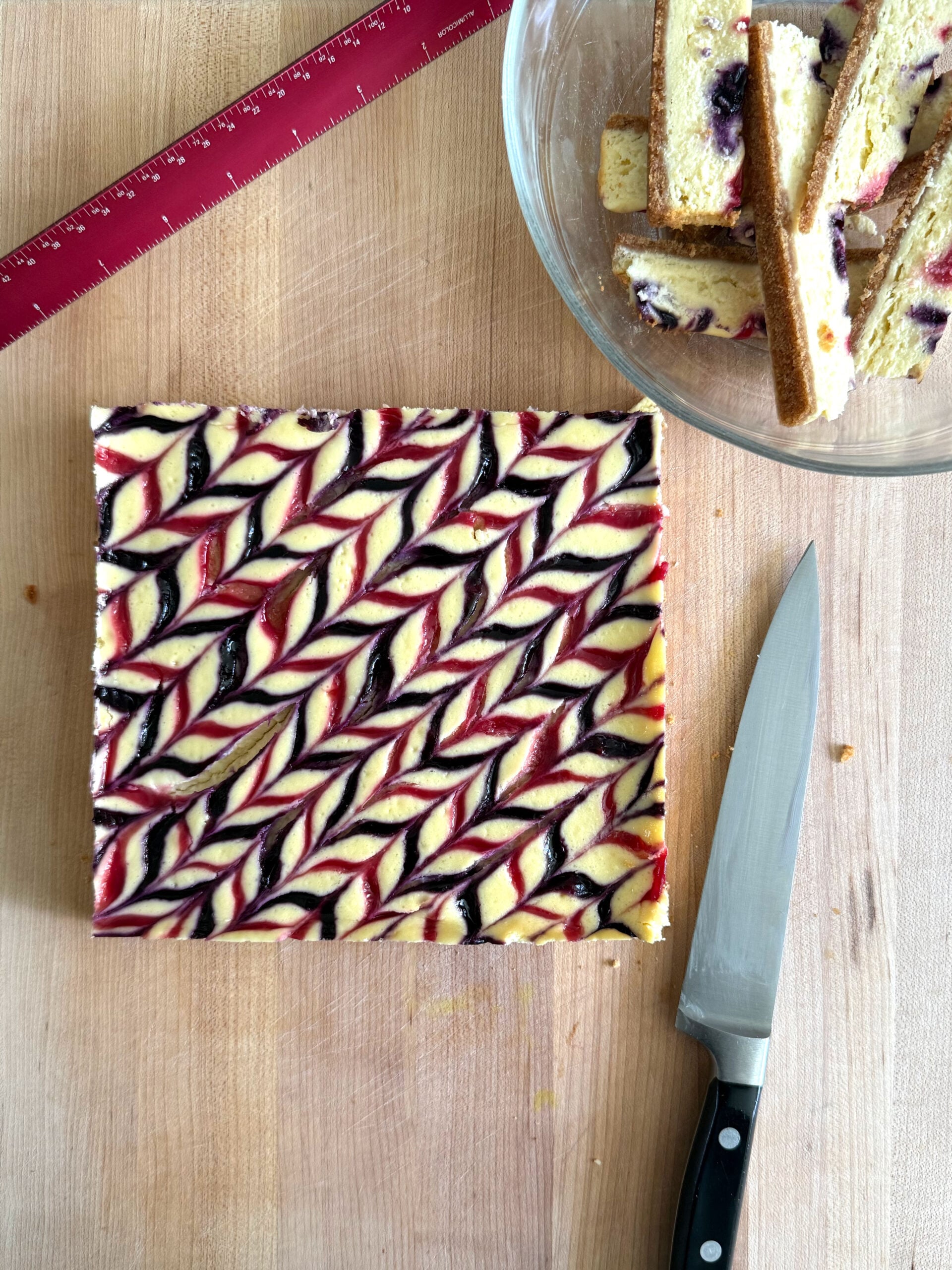 Unmolded cheesecake on cutting board with edges trimmed off. Ready to be cut using a ruler to make even squares.
