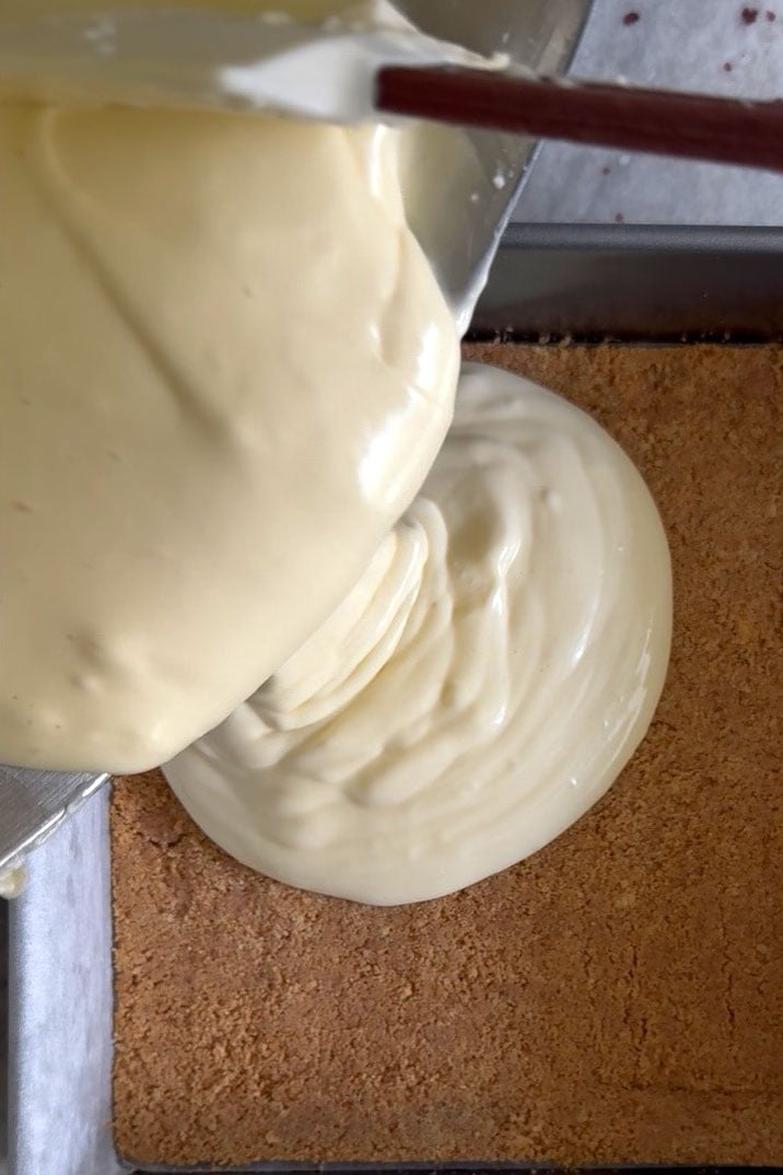 Cheesecake batter being poured ove cooked crust.