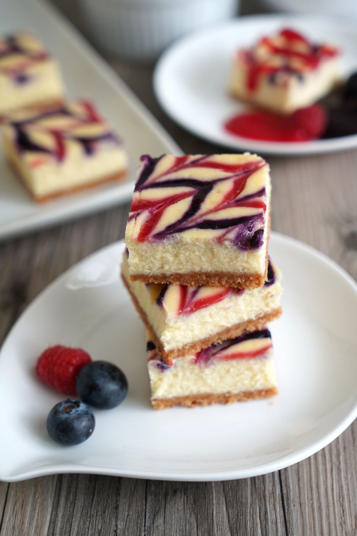 Threee cheesecake bars stacked on white plate.
