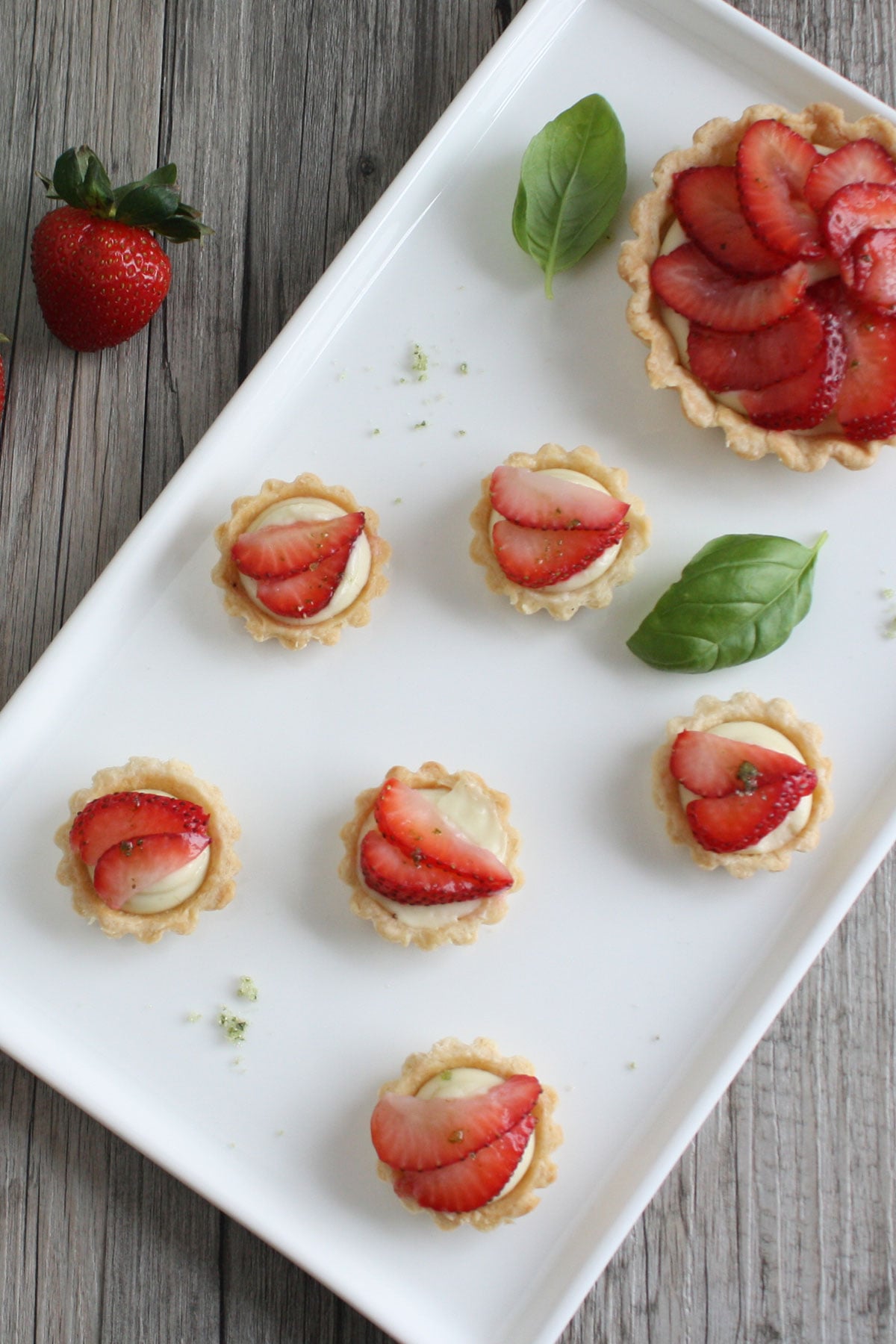 Mini strawberry basil cream tarts on a white plate. 