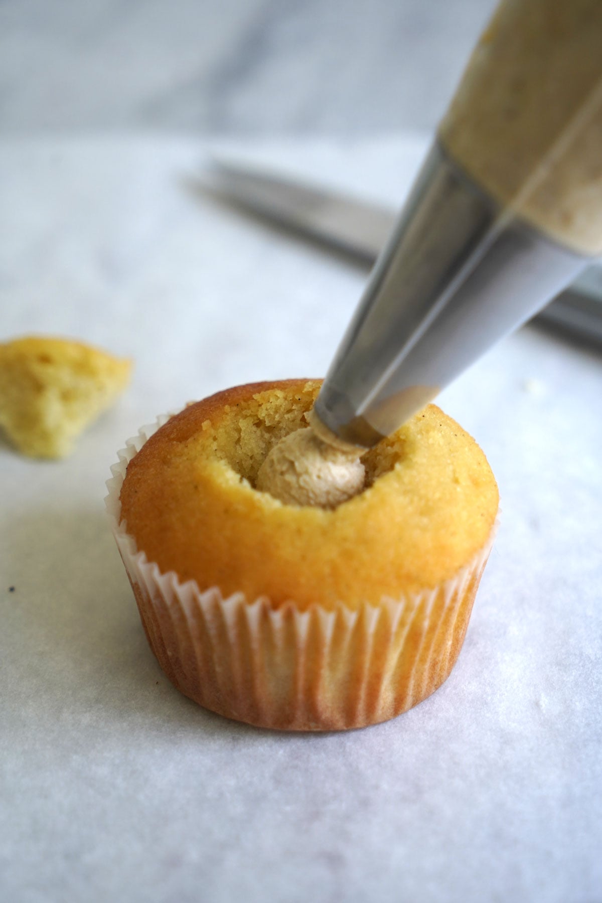 Espresso pastry cream being piped into inside of cupcake.