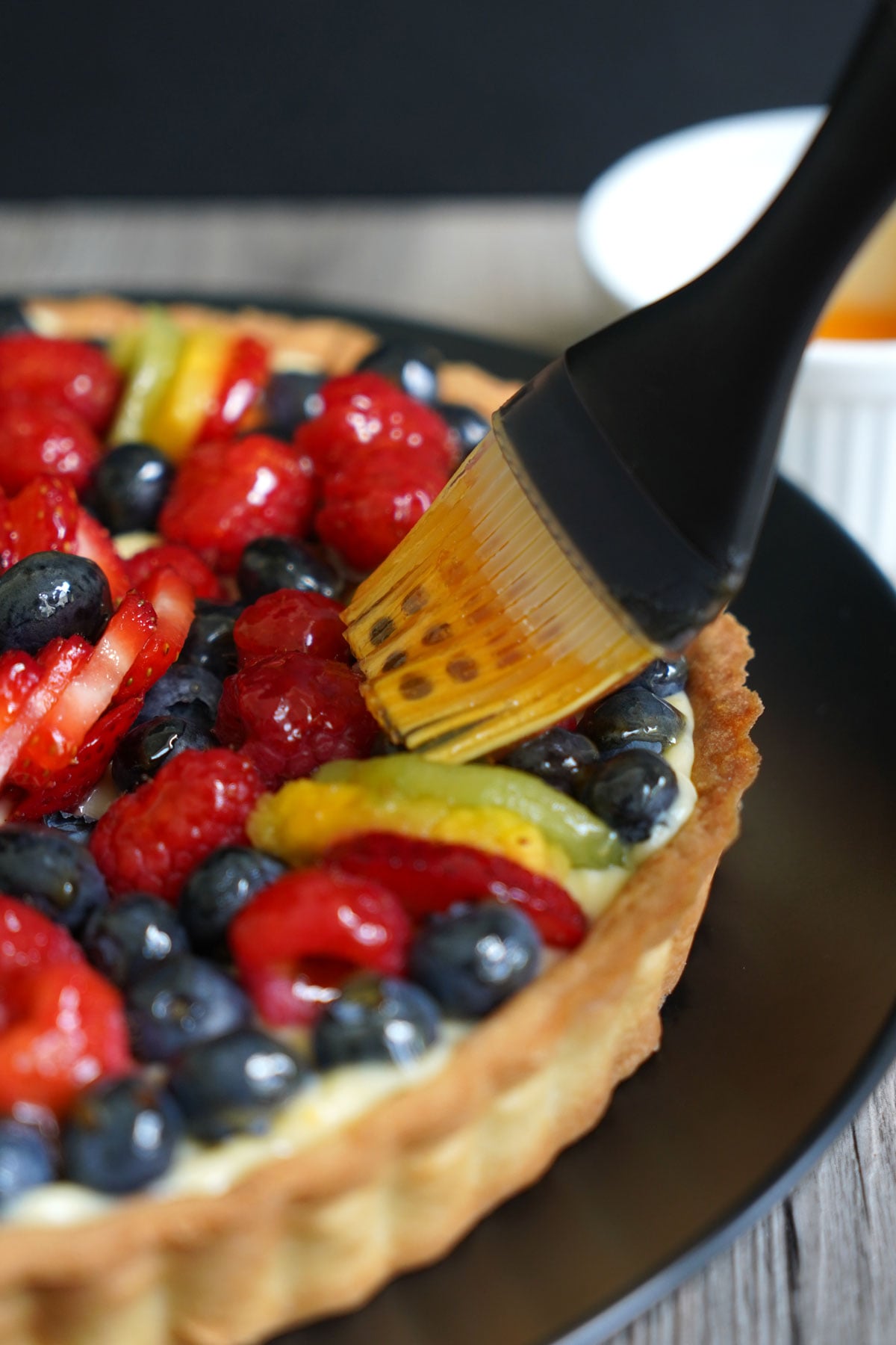 A fruit tart being glazed with a pastry brush.