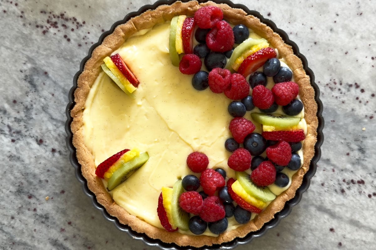 Fruits being arranged on the fruit tart.
