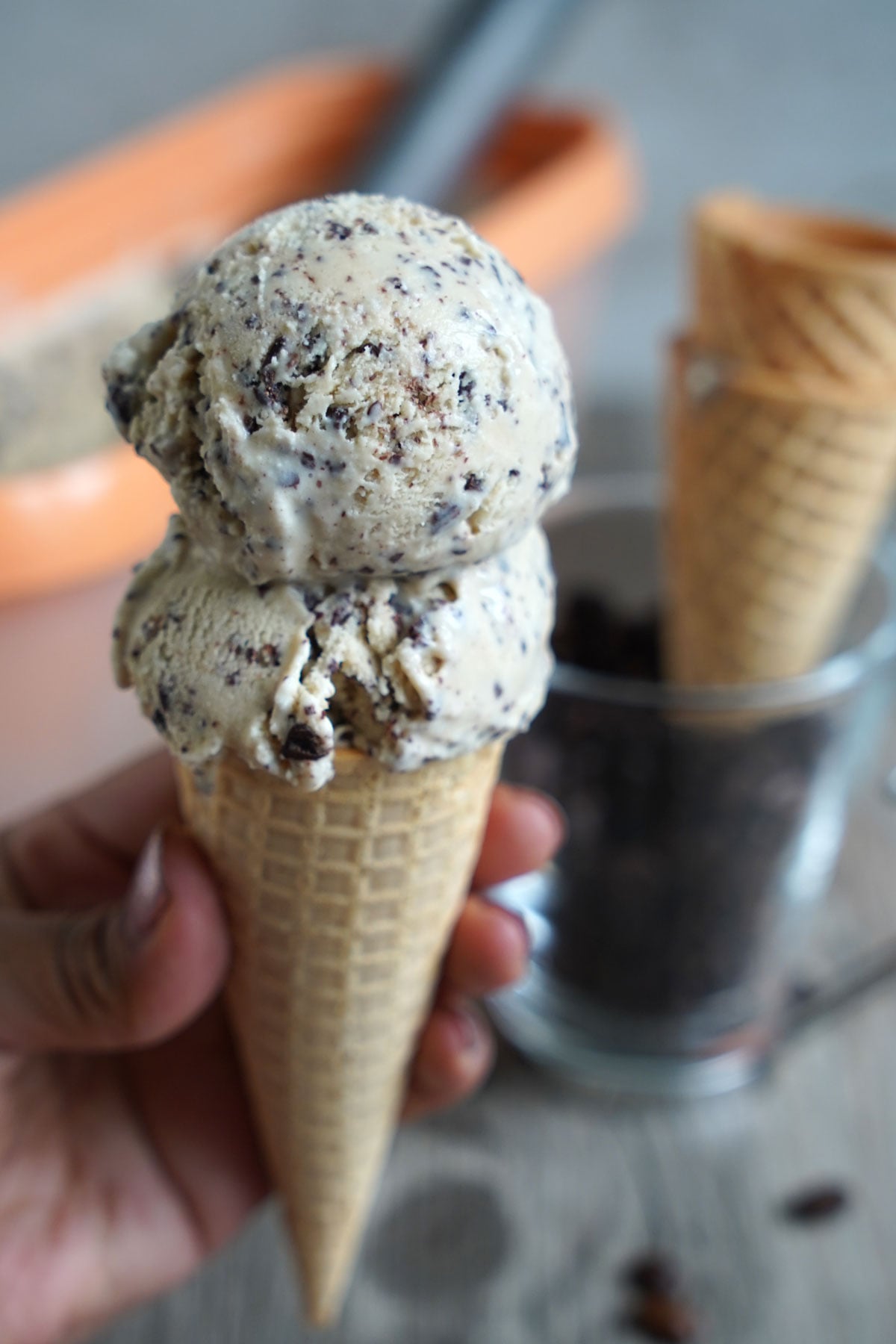 Two scoops of espresso ice cream in a cone being held by a hand.