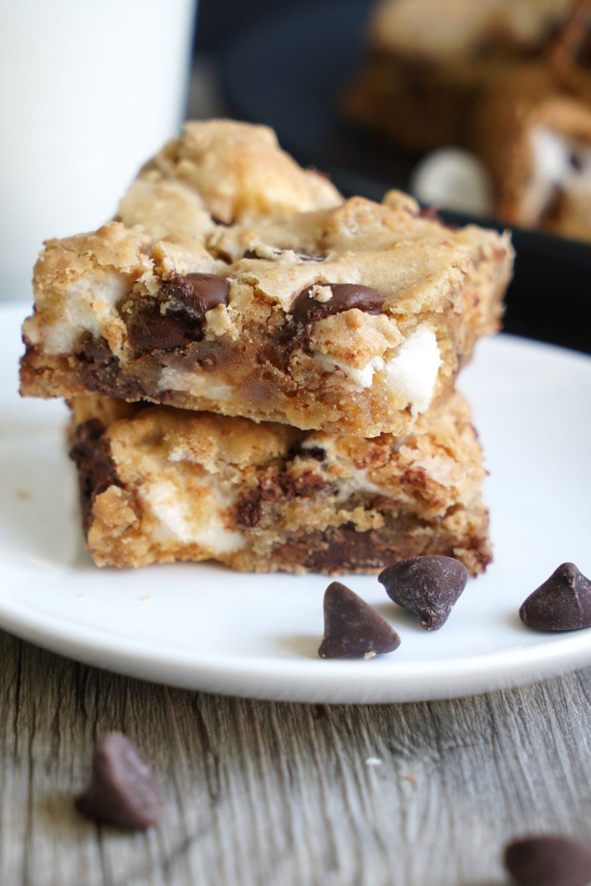 S'mores cookie bars stacked on white plate with milk in background. Close up view.