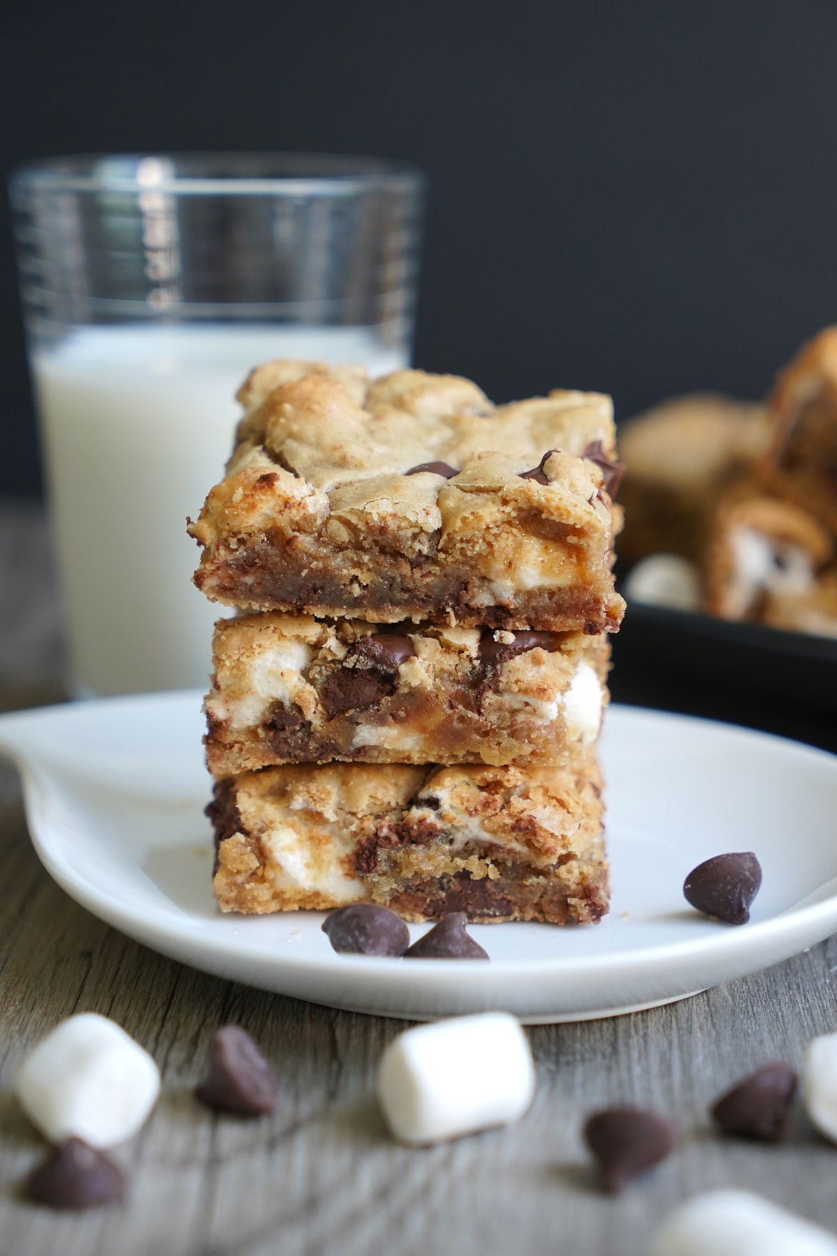 S'mores cookie bars stacked on white plate with milk in background.