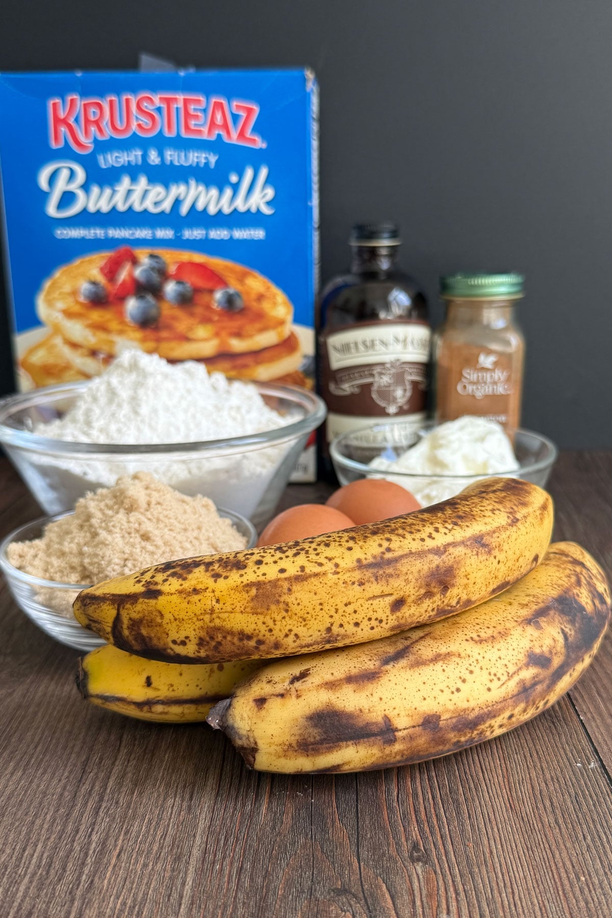 Ingredients for making pancake mix banana bread. Showing overripe bananas, brown sugar, Krusteaz pancake mix, vanilla, cinnamon and greek yogurt.