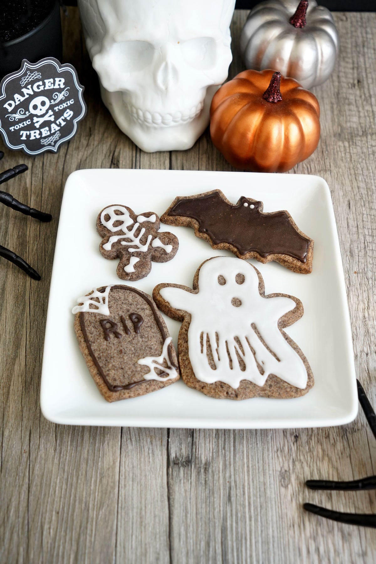 Halloween sugar cookies shaped like a bat, ghost, skeleton, and tombstone on a white plate