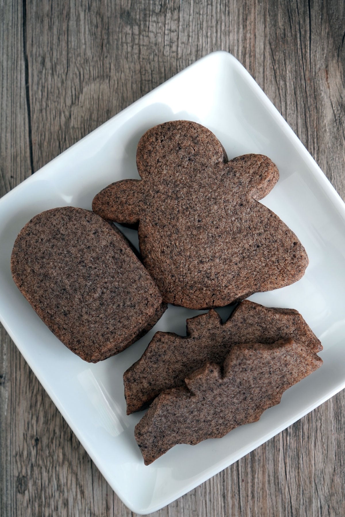 Undecorated Halloween sugar cookies shaped like a bat, ghost, and tombstone on a white plate