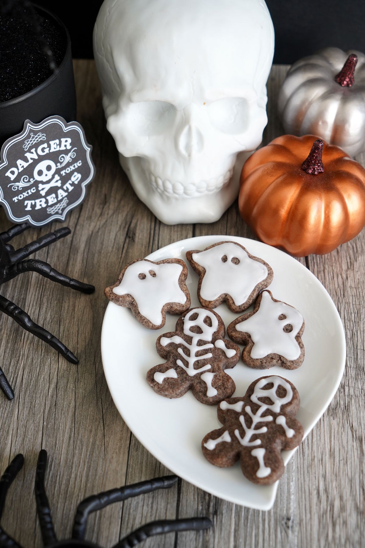 Small skeleton cookies and mini ghost shaped cookies piped with white icing lines on speckled Oreo dough.
