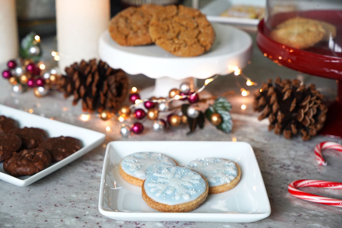 Cookie swap table with decorated snowflake cookies, gingersnaps and mocha almond cookies.
