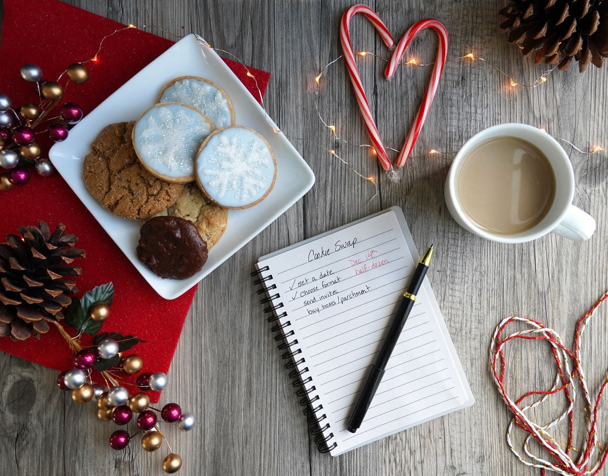 Planning a cookie swap: Notebook and pen with coffee, plate of cookies in a flat lay. 